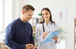 © Studio Romantic - Portrait of a young man patient in medical office listening to a friendly female doctor holding report file with appointment and giving consultation during medical examination in clinic.