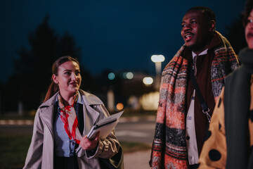 Wall Mural - Three colleagues are seen outdoors at nighttime, carrying materials and talking in an engaged manner, emphasizing collaboration, diversity, and teamwork during a professional occasion.