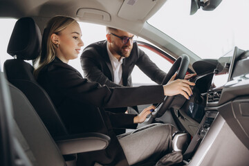 Wall Mural - Happy adult female buyer - business woman - enjoying buying a new, modern car at a car dealership. The concept of an expensive purchase, rental and test drive.