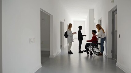 Poster - Students engaging in conversation with wheelchair using classmate, showcasing inclusive interaction along white corridor during academic setting in slow motion