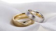 © peco - 金と銀のペアの結婚指輪が、白いサテン生地の上にエレガントに並べられています