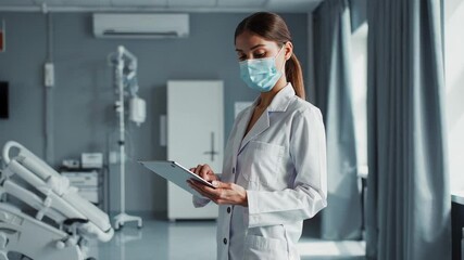 Aufkleber - Professional medical worker reviewing patient data on tablet while standing in hospital room, surrounded by medical equipment and wearing protective mask
