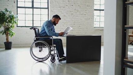 Aufkleber - Professional worker navigating workplace with wheelchair, reading documents at modern desk, demonstrating independence and skill through focused concentration