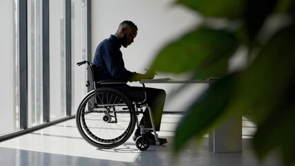 Aufkleber - Office worker using a wheelchair taking notes at his desk in a bright office space next to large windows, captured in a slow motion sequence