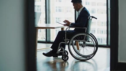 Aufkleber - Businessman in wheelchair using digital tablet near window in modern office, slow motion video showcasing accessibility and inclusion in workplace