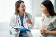 © Parichat - Female medical professional reviewing patient records, providing healthcare guidance and support while standing near hospital bed, emphasizing doctor-patient communication