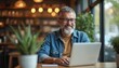© Vadym - Bearded man using laptop in cafe. Businessman works online. Smiling adult types on computer. Confident freelancer connects cyberspace at table. Happy person communicates at workplace. Remote job