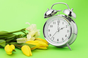 Poster - Spring time. Alarm clock and beautiful flowers on green background