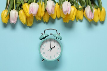 Poster - Spring time. Alarm clock and beautiful tulips on light blue background, flat lay