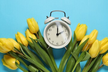 Poster - Spring time. Alarm clock and beautiful tulips on light blue background, flat lay