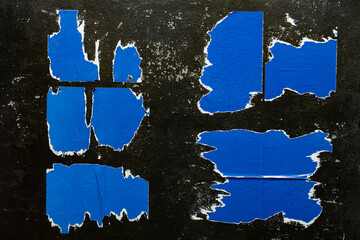 Poster - Scraps of a blue poster on a black wall.