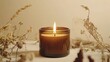 © Alien - Minimalist composition of a burning candle in a brown glass jar, surrounded by dried plants, creating a warm and cozy atmosphere.