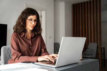 Canvas Print - Focused young adult female freelancer financial specialist in eyeglasses typing on laptop computer, working from home. Successful business woman entrepreneur using pc for online remote freelance work 