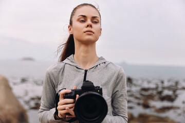 Female photographer on the beach holding a camera, dressed in casual sportswear, exuding confidence and focus with a moody ocean background