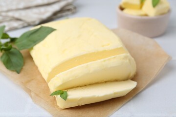 Wall Mural - Cut brick of butter and basil on white table, closeup