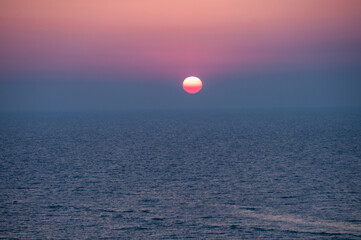 A beautiful sunset over the ocean with a large red sun in the sky