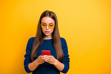 Portrait of concentrated lady in eyewear eyeglasses holding device wearing burgundy jumper isolated over yellow background