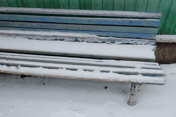 Aufkleber - A wooden bench covered in snow sits next to a building on a cold winter day.