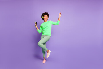 Wall Mural - Full length body size photo of trendy stylish cute free girlfriend wearing green pants trousers yellow sweater footwear in headphones listening to music dancing isolated violet pastel color background