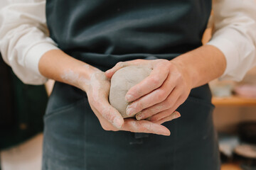 Poster - Girl potter is creating a ceramic ware in the workshop. Woman potter works with wet clay in the pottery studio.