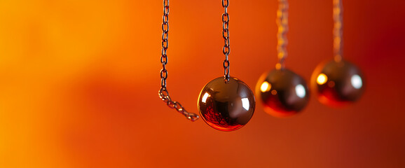 Poster - Close-up view of three metallic spheres suspended by chains against an orange background, symbolizing motion, energy, balance, and reflection with smooth metallic surfaces.