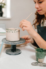 Fototapete - Artist is decorating and painting handmade ceramic clay cup in the creative workshop. Painter is drawing and adding unique designs to the earthenware.
