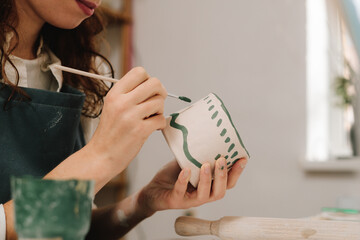 Poster - Painter is drawing and making a colorful decoration of a clay ware. Female artist is painting earthenware with paintbrush and water colors in the workshop.
