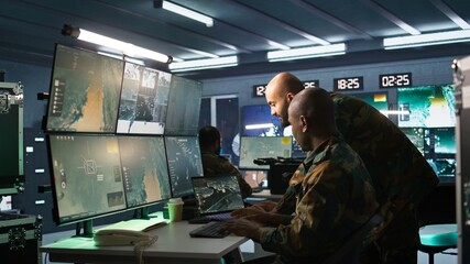 Poster - Military soldier in mission control center, overseeing national safety operations using notebook next to colleague. Team of army specialists examining data in monitoring room command center, camera B