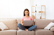 © Prostock-studio - Frontal portrait of happy girl chatting online on laptop with friend at home, sitting on beige couch in light living room