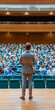© Narongsak - A speaker stands confidently on stage, addressing a large audience in a beautifully designed auditorium.