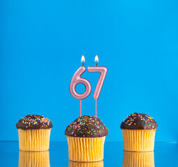 Wall Mural - Birthday candle with the number 67 - Three cupcakes on a blue background.