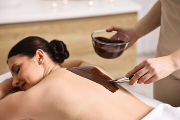 Wall Mural - Chocolate body wrap. Spa worker applying mask onto woman's back in salon, closeup