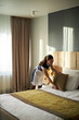 © DragonImages - Housekeeper arranging pillows and smoothing blankets on bed in well-lit hotel room with large window and curtains, ensuring cleanliness and comfort for guests