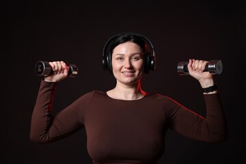 Wall Mural - Plus size woman in gym clothes with dumbbells and headphones on black background