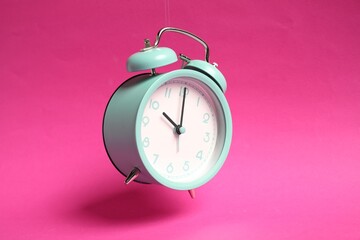 Wall Mural - Turquoise alarm clock in air on bright pink background