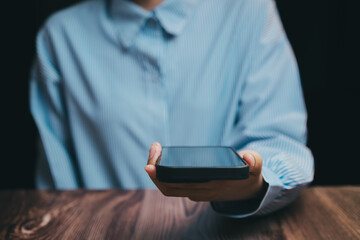 Poster - Person Holding Smartphone in Dark Background with Wooden Table, Business concept