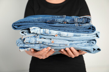 Wall Mural - Woman with stack of different stylish jeans near light wall indoors, closeup