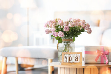 Calendar with date of International Women's Day, roses and gift box on table in bedroom, closeup