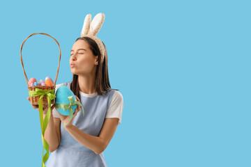 Sticker - Young woman in bunny ears with basket of Easter eggs blowing kiss on blue background