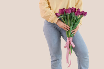 Canvas Print - Young woman with bouquet of beautiful purple tulips on beige background, closeup