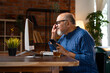 © StockImageFactory - Indian elderly man in kurta works on desktop, talks on the phone, and drinks coffee at home