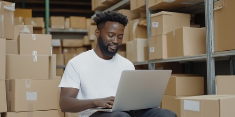 Wall Mural - A man is sitting on a pile of boxes and using a laptop. He is smiling and he is enjoying himself