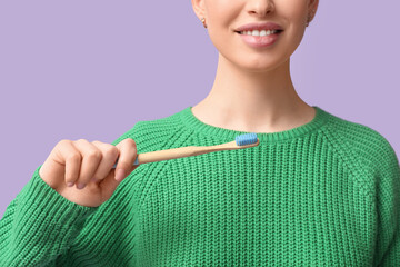 Young woman with toothbrush on lilac background, closeup