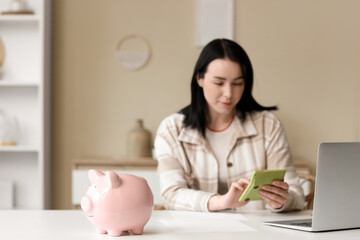 Wall Mural - Piggy bank on table against woman calculating refund at home, closeup