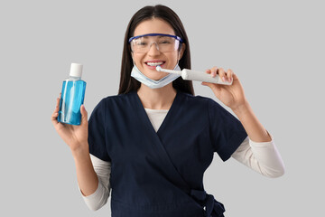 Poster - Young female dentist with electric toothbrush and mouth rinse on light background