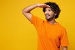 © ViDi Studio - Young smiling cheerful happy Indian man he wearing orange t-shirt casual clothes hold hand at forehead looking far away distance isolated on plain yellow background studio portrait. Lifestyle concept.
