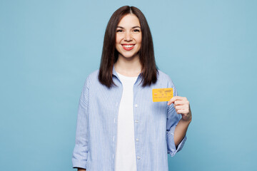 Canvas Print - Young smiling happy fun Caucasian woman she wears shirt casual clothes hold in hand mock up of credit bank card isolated on plain pastel light blue cyan background studio portrait. Lifestyle concept.