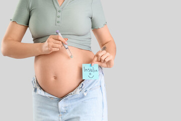 Wall Mural - Young pregnant woman holding paper with word INSULIN and lancet pen on light background. Gestational diabetes concept