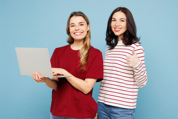 Young IT couple two friends women wearing red casual clothes together hold use work on laptop pc computer show thumb up isolated on pastel plain light blue cyan background studio. Lifestyle concept.