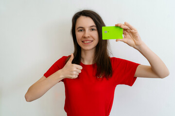 smiling young brunette woman wears basic red t-shirt hold in hand credit bank card show thumb up ges